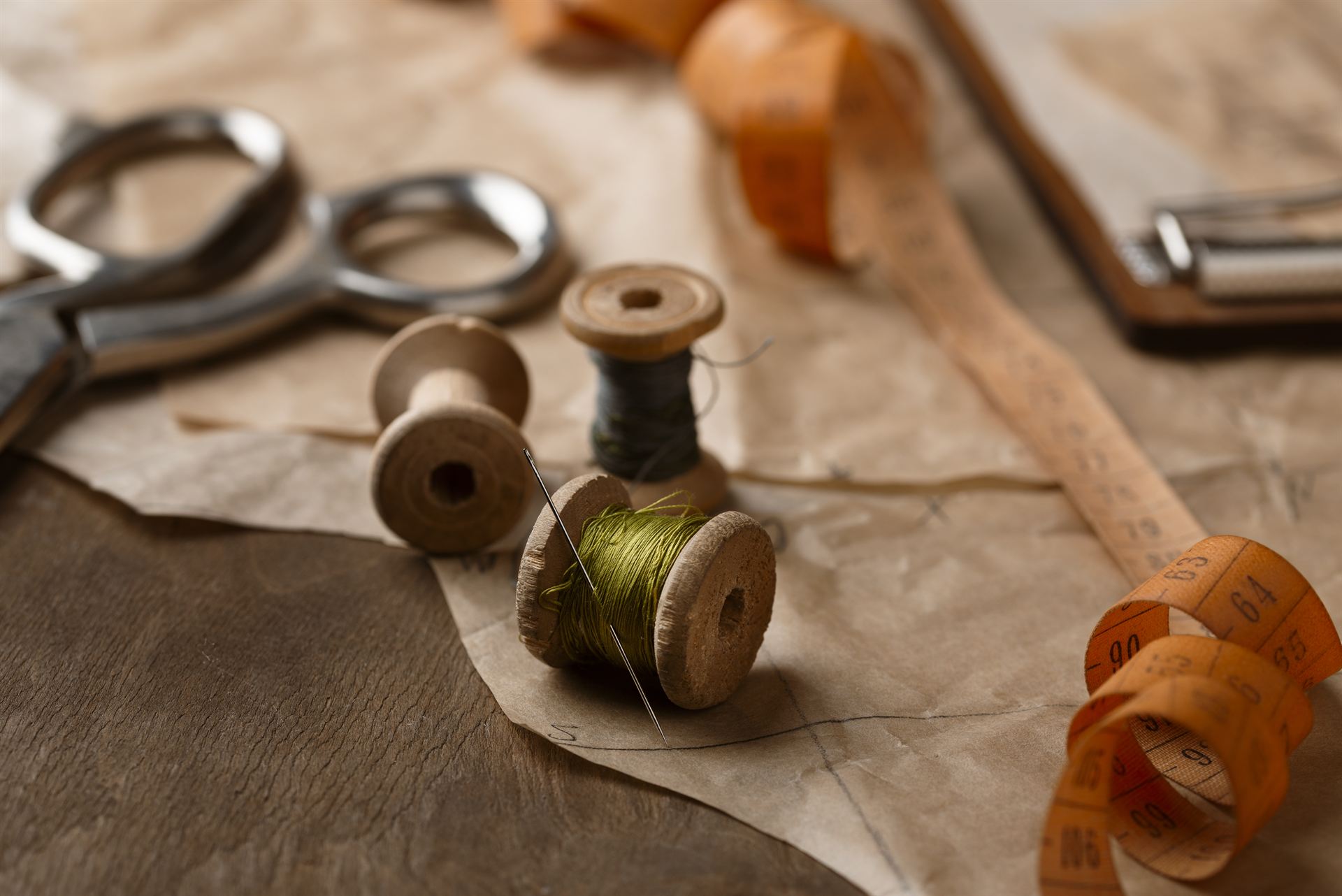 Wooden thread spools, a needle, scissors and a measuring tape on the workroom bench